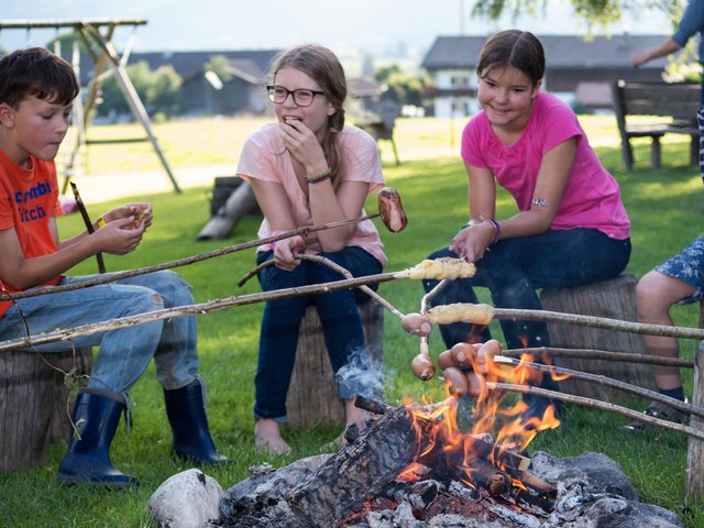Kinder sitzen abends am Lagerfeuer und grillen Stockbrot 