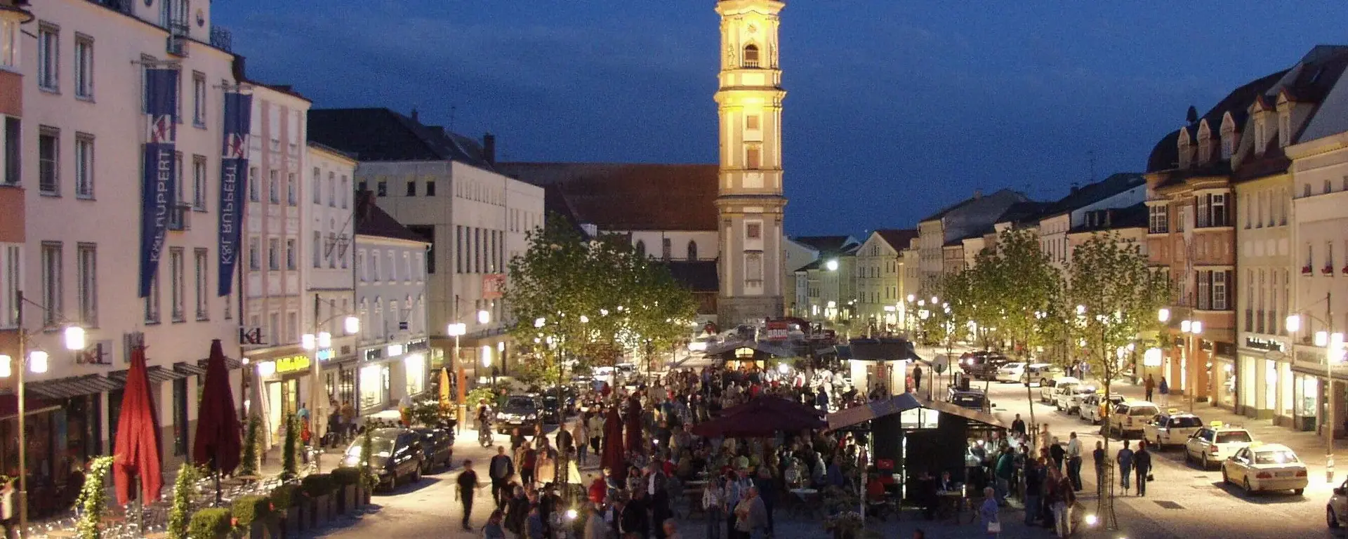 Sicht auf den beleuchteten Luitpoldplatz bei Nacht   an dessen Ende der Kirchenturm zu sehen ist 